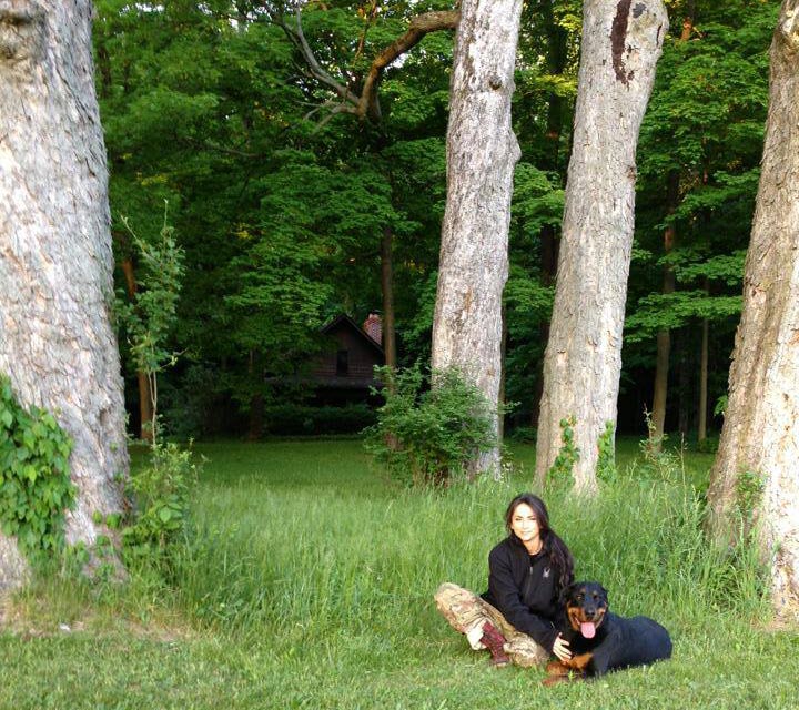 Nicole McClain sits in the woods with her Rottweiler Mogador Frankenstein McClain